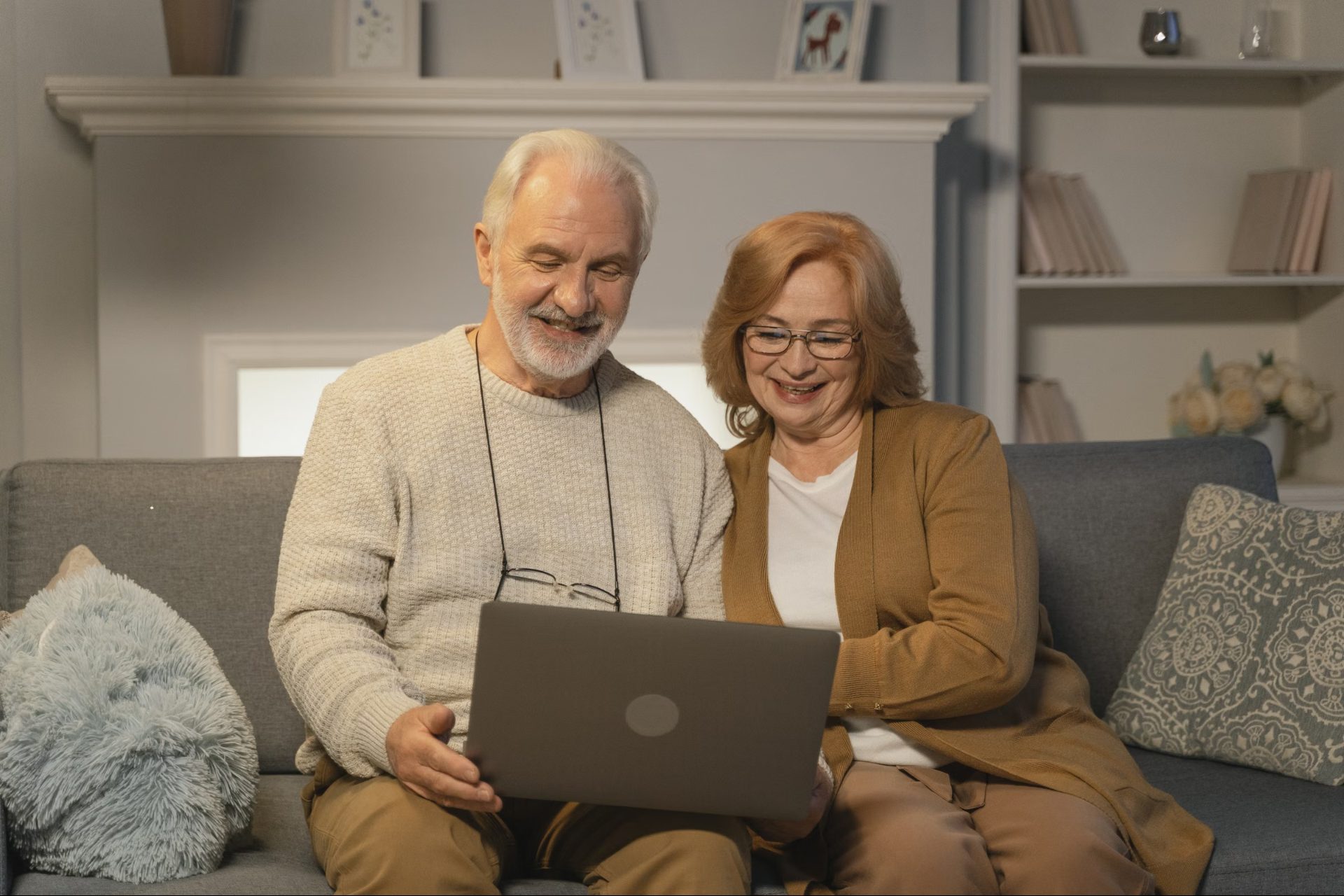 A retired couple smiling while looking at a laptop on their sofa