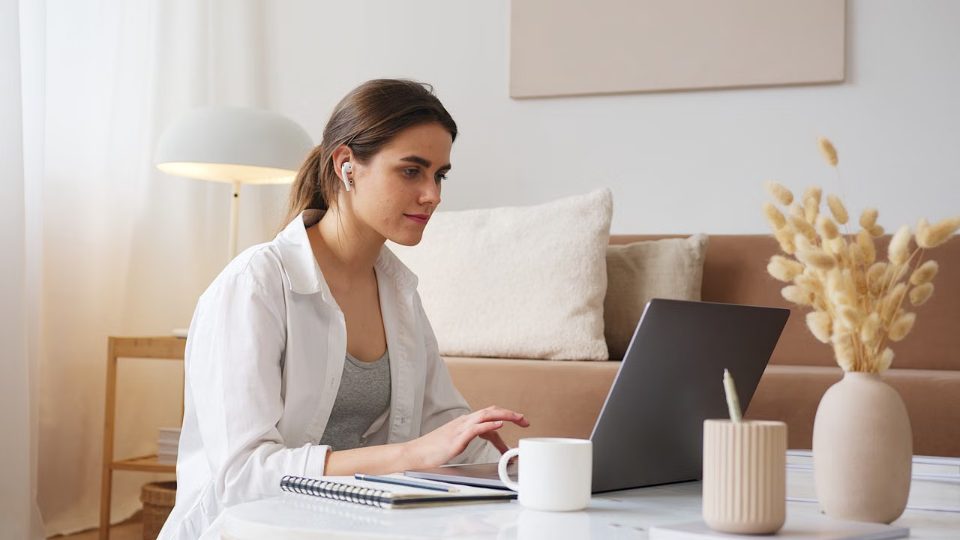 A woman working on a laptop at a bright home desk